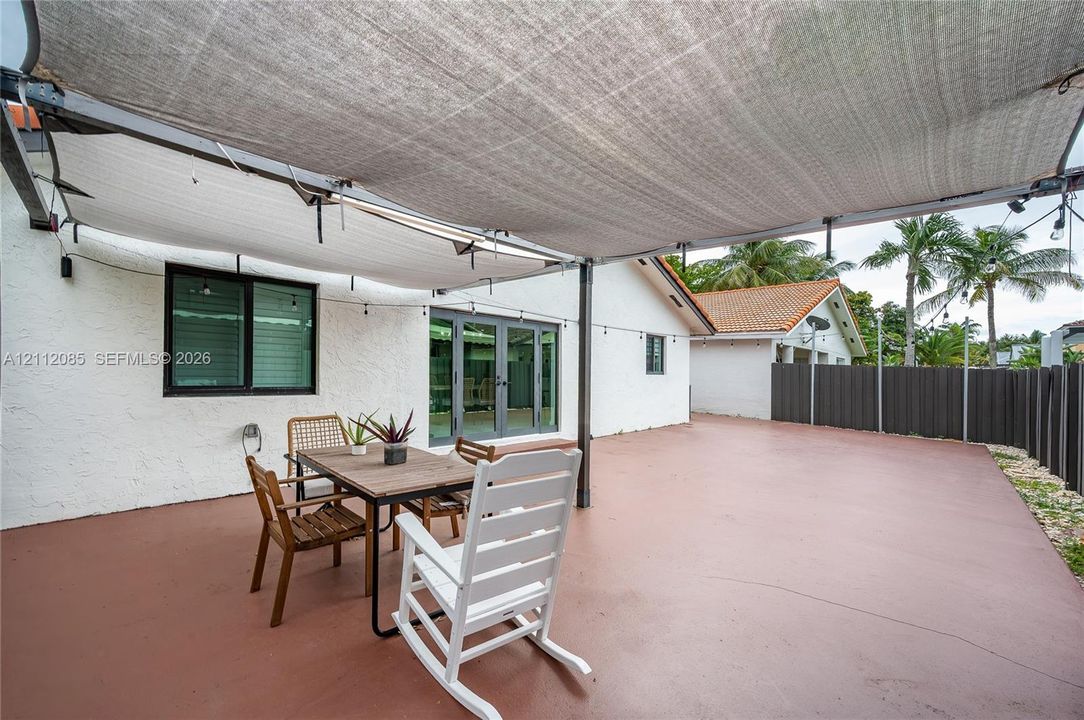 Outdoor patio featuring painted concrete flooring, a metal-framed overhead shade structure, and multi-panel glass entry doors