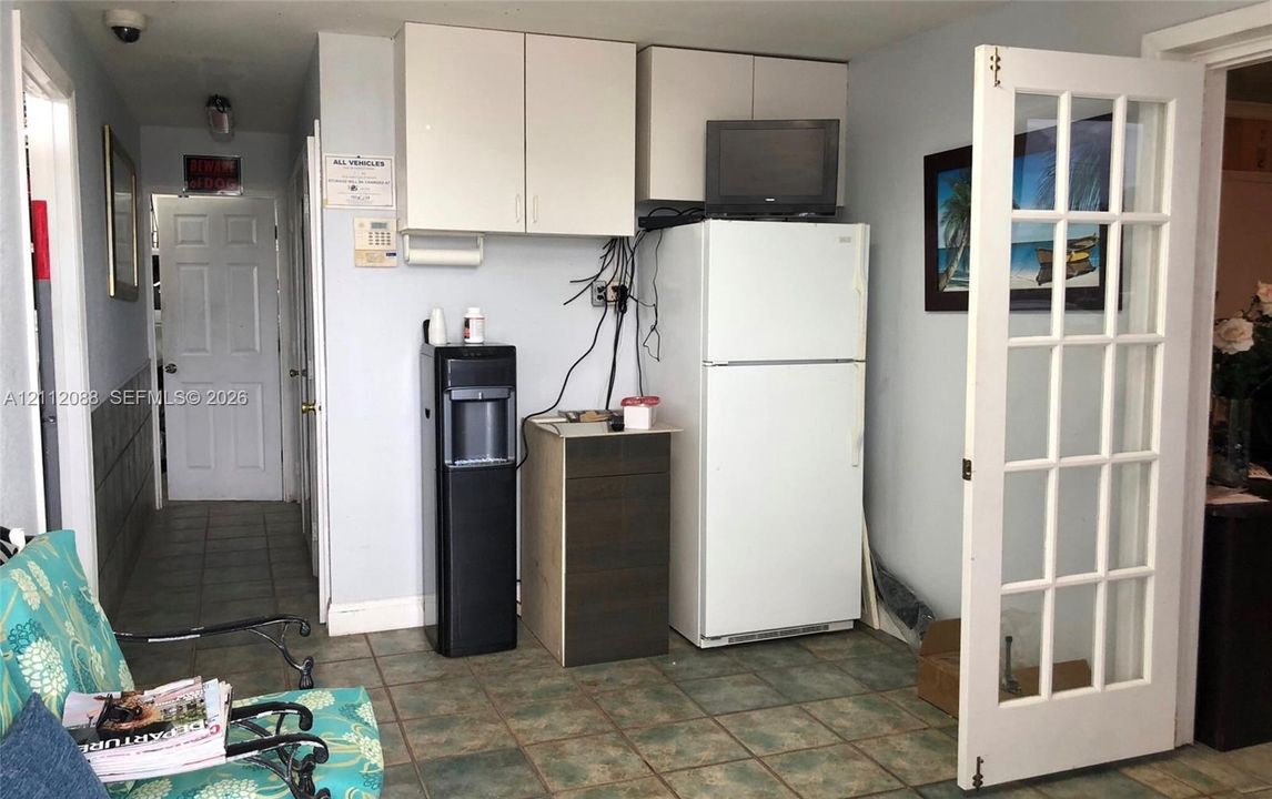 Wall-mounted white cabinetry, full-size white refrigerator, tile flooring, and a multi-pane French door