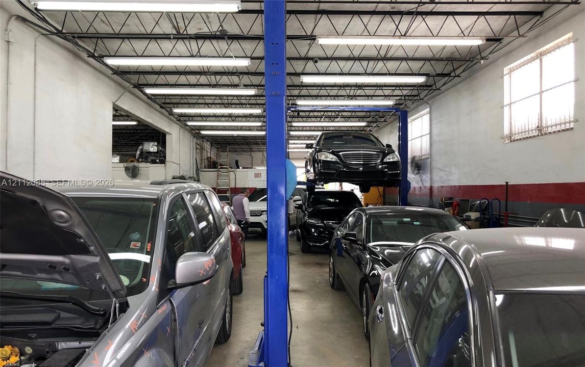 Expansive workshop interior featuring high, exposed-beam ceilings, industrial-grade concrete flooring, full-length fluorescent overhead lighting, and an installed hydraulic vehicle lift