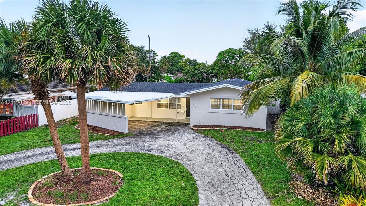 Single-story residence featuring a covered carport, crisp white exterior finish, multi-pane windows, and mature palm landscaping situated on a manicured lawn