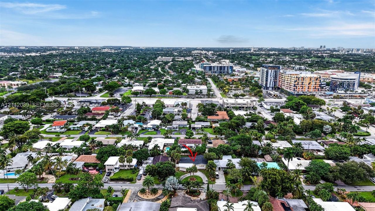 Aerial perspective featuring a single-story residence with a pitched roof, circular driveway, mature landscaping, and an enclosed backyard