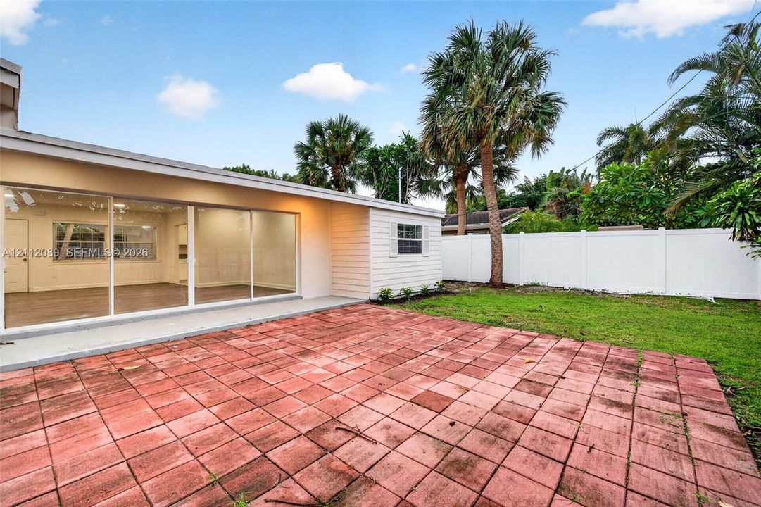Backyard featuring a red paver patio, white vinyl privacy fencing, and mature palm trees