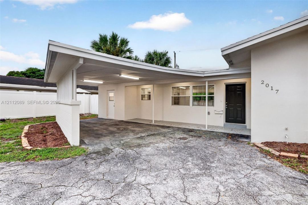 Exterior featuring a covered carport, recessed lighting, solid entry door, and perimeter vinyl fencing