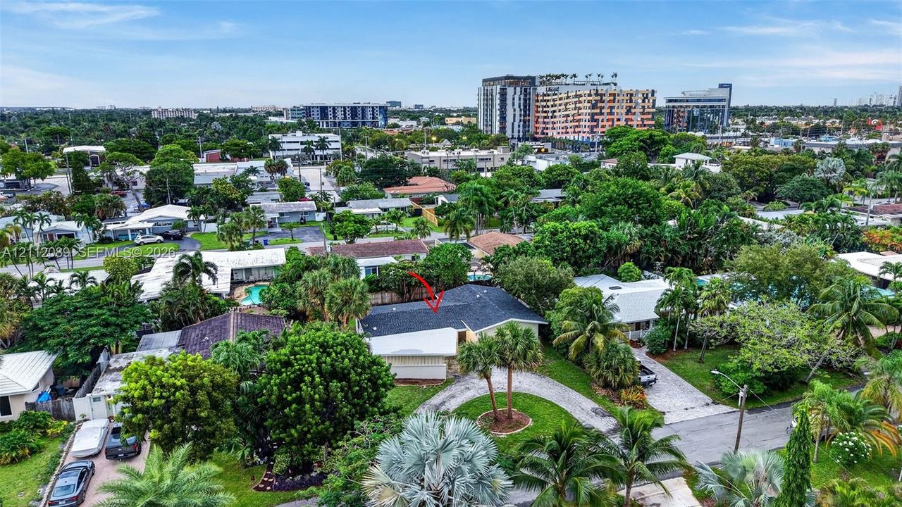 Aerial perspective of a residential property featuring a dark-toned shingled roof, a curved driveway, and established palm trees within a landscaped lot