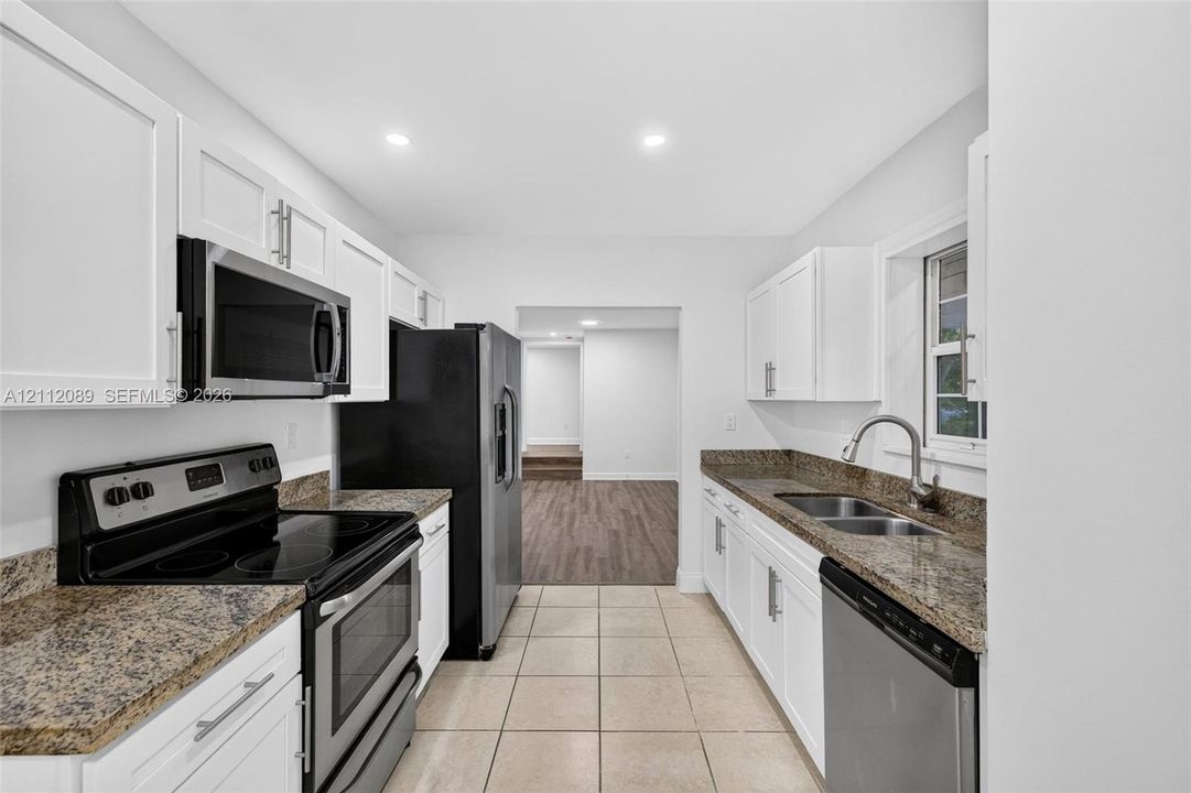 Kitchen featuring white Shaker-style cabinetry, stone countertops, dual-basin stainless steel sink, and stainless steel appliances including a microwave, range, and dishwasher