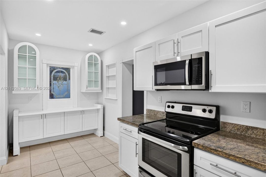 White Shaker-style cabinetry, stone-finish countertops, stainless steel appliances, arched glass-panel wall cabinetry, and tile flooring