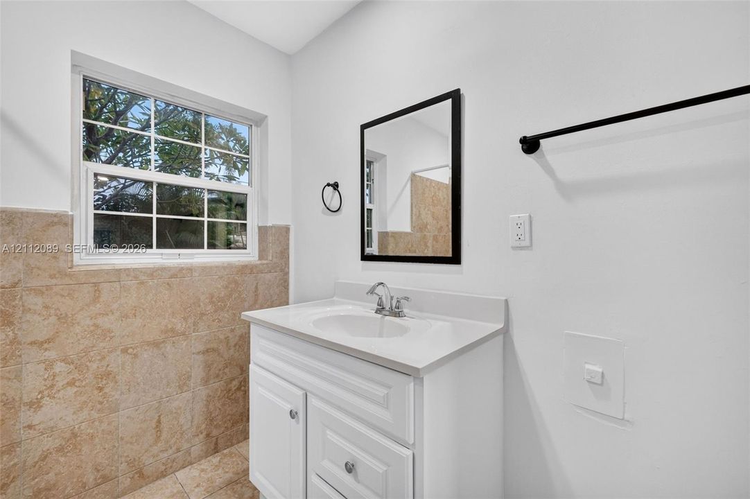 Single-sink vanity with a solid-surface countertop, neutral tile wainscoting, framed wall mirror, and matte black hardware