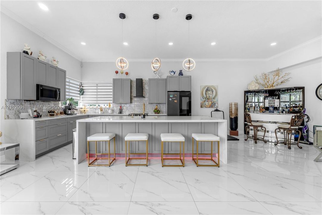 Kitchen featuring light-gray shaker-style cabinetry, quartz countertops, a stone-tile backsplash, polished large-format tile flooring, and three contemporary spherical pendant lights suspended over a central island