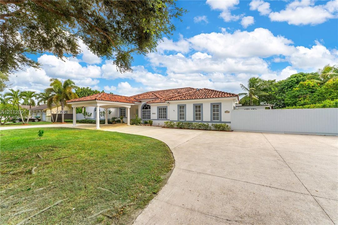 Single-story residence featuring a clay tile roof, covered porte-cochère, multi-pane windows, expansive concrete motor court, and perimeter privacy fencing