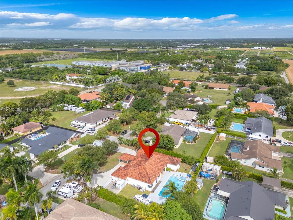 Aerial perspective featuring a single-story residence with a multi-hipped terracotta tile roof, an in-ground swimming pool, concrete paved patio area, and mature perimeter landscaping