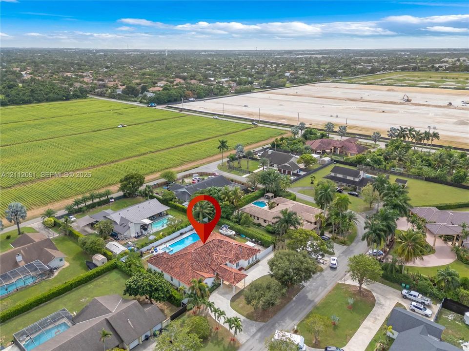 Aerial perspective of a property featuring a multi-hipped tile roof, an expansive paved driveway, and a private rear swimming pool