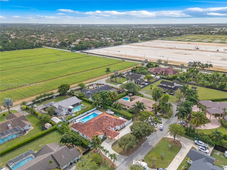 Aerial perspective of a sprawling property featuring a multi-gabled terracotta tile roof, a rectangular swimming pool, an expansive paver driveway, and mature landscaping