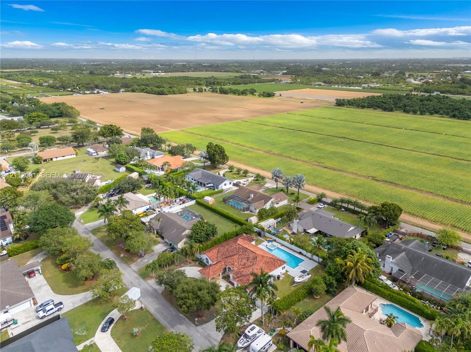 Aerial perspective of a sprawling residential property featuring a clay tile roof, a private swimming pool, concrete hardscaping, and mature palm trees
