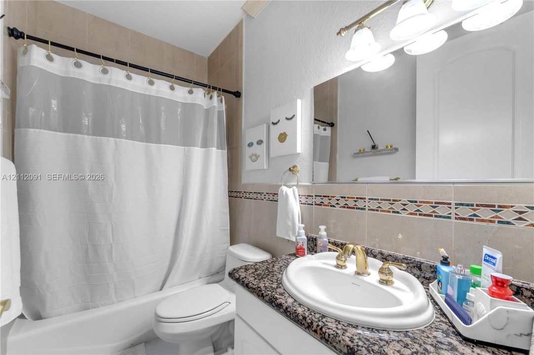 Bathroom featuring a stone-surface vanity countertop, drop-in sink with brass-toned hardware, decorative tile backsplash, and a tub-shower combination with full-height tile wall surround