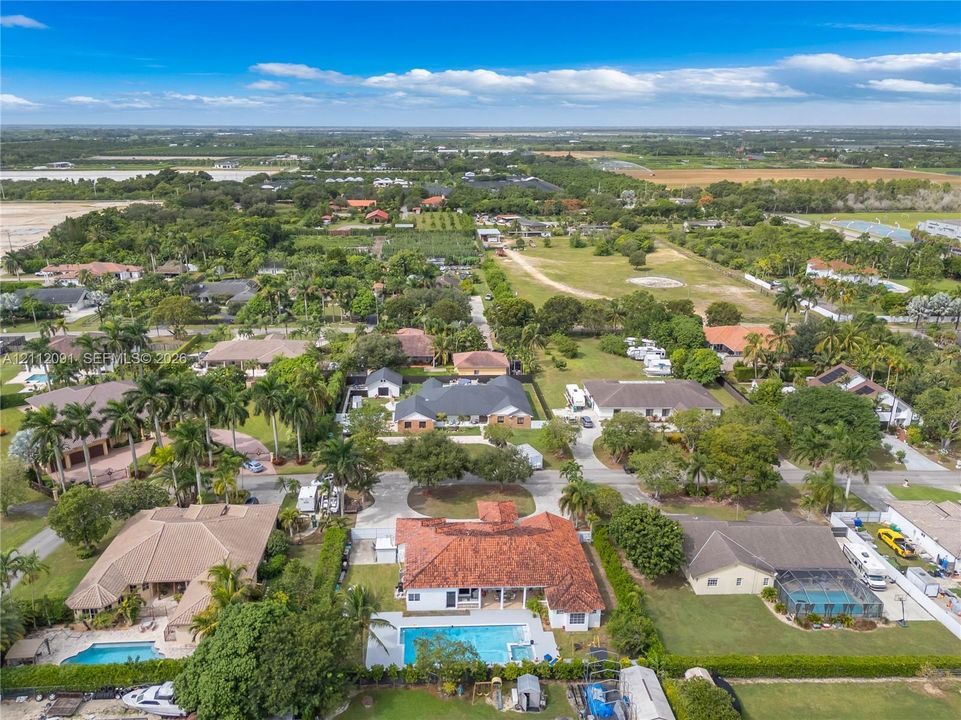 Aerial perspective of a residential property featuring a multi-hipped clay tile roof, a rectangular in-ground swimming pool, a concrete patio area, and mature landscaping