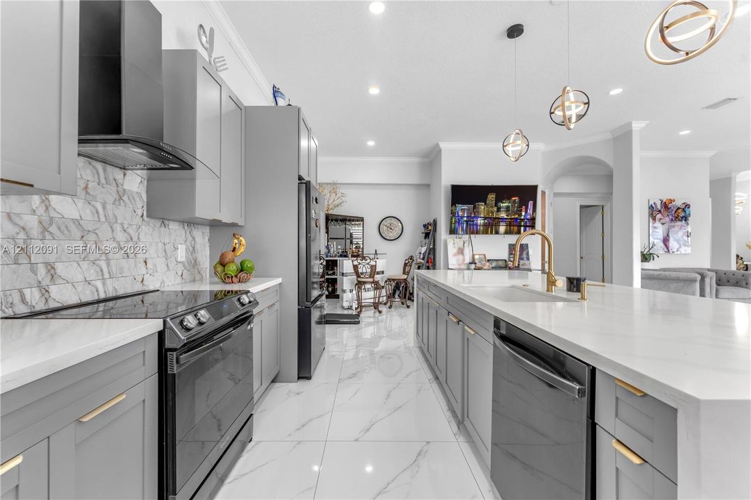 Kitchen featuring gray shaker-style cabinetry, a stone-pattern backsplash, quartz countertops, a central island with a gold-finish faucet, and large-format porcelain tile flooring