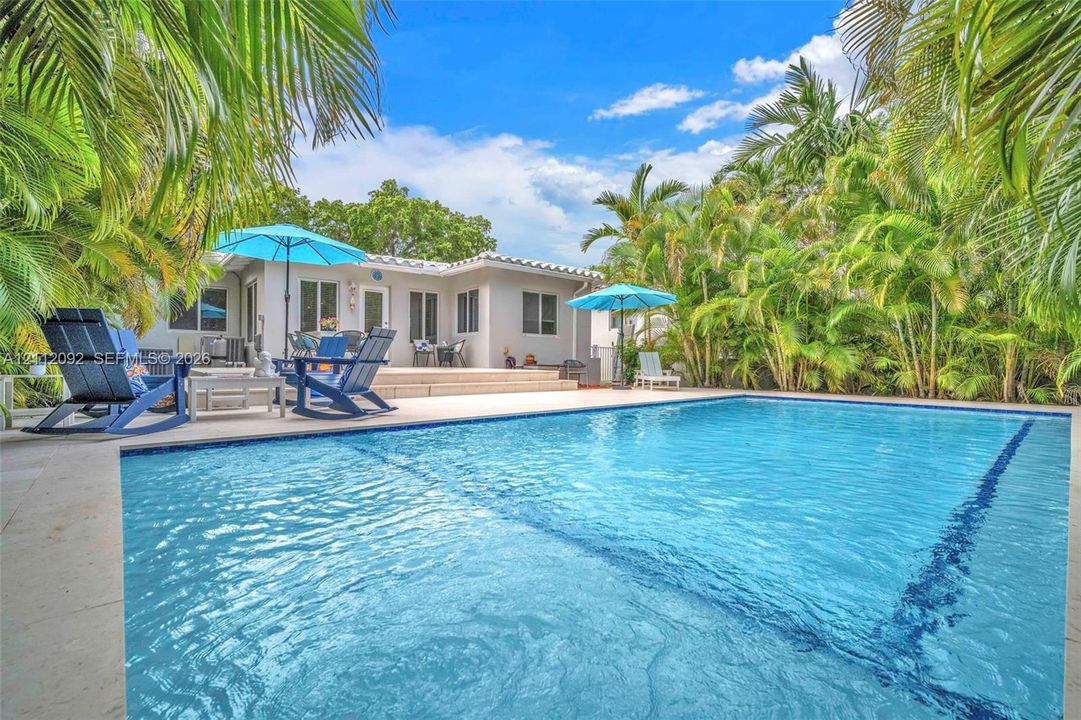 In-ground swimming pool with a tiled perimeter, expansive stone-finish patio, and mature palm landscaping