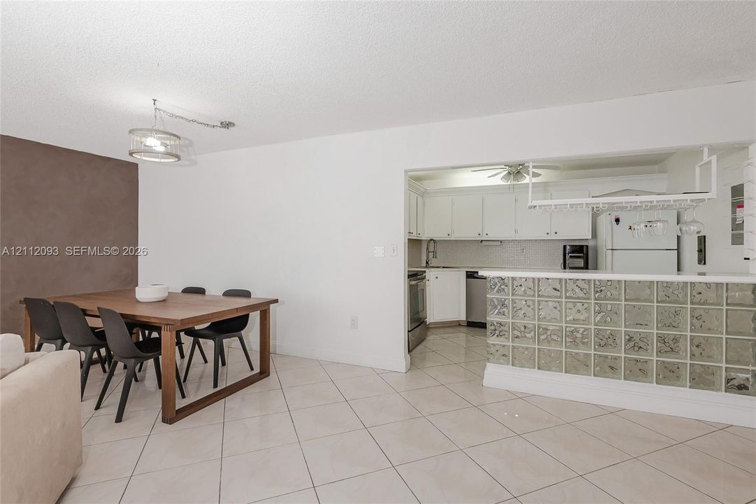 Dining area featuring a dark-toned accent wall and a drum-style pendant light, kitchen with white cabinetry, glass block breakfast bar, and diagonal tile flooring