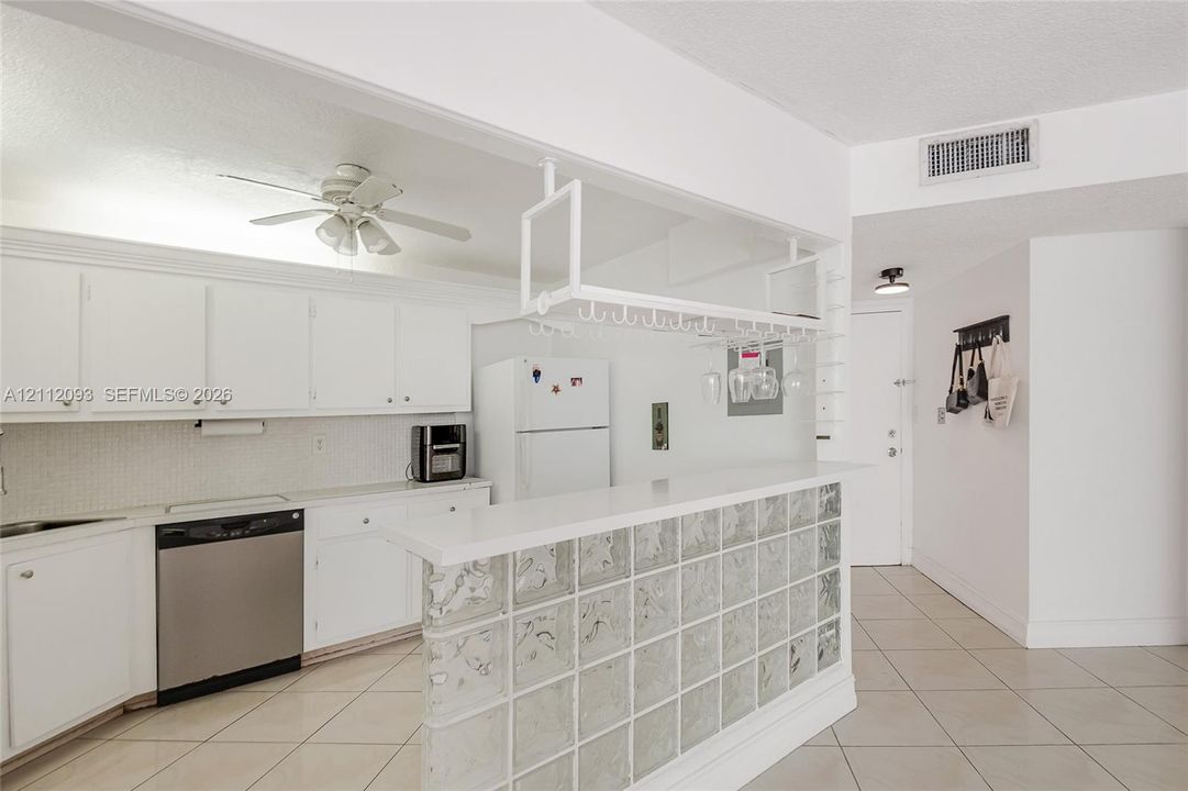 Kitchen featuring white cabinetry, solid-surface breakfast bar with a glass block base, overhead stemware rack, and tile flooring