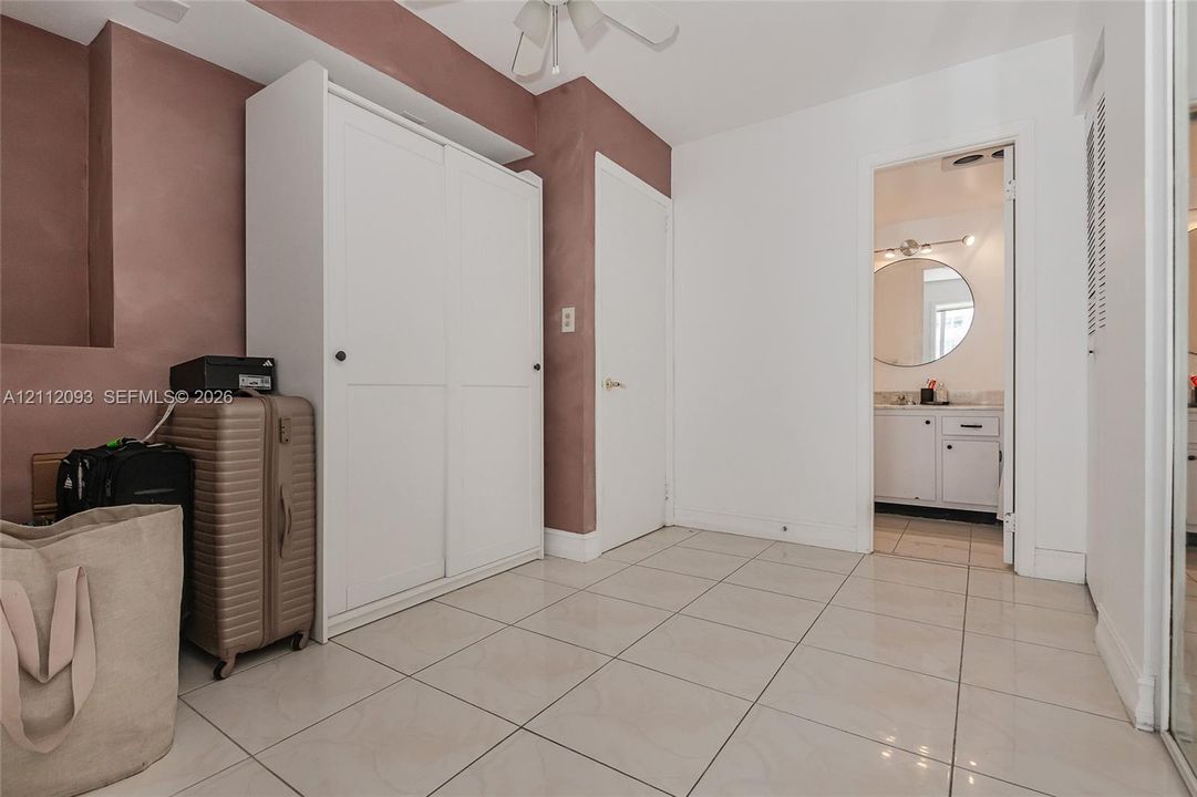 Large-format neutral floor tiling, built-in white wardrobe cabinetry, and recessed ceiling lighting