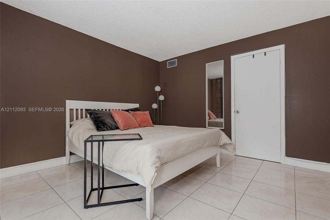 Room featuring neutral wall tones, large-format tile flooring, a solid-core interior door, and a built-in wall-recessed mirror