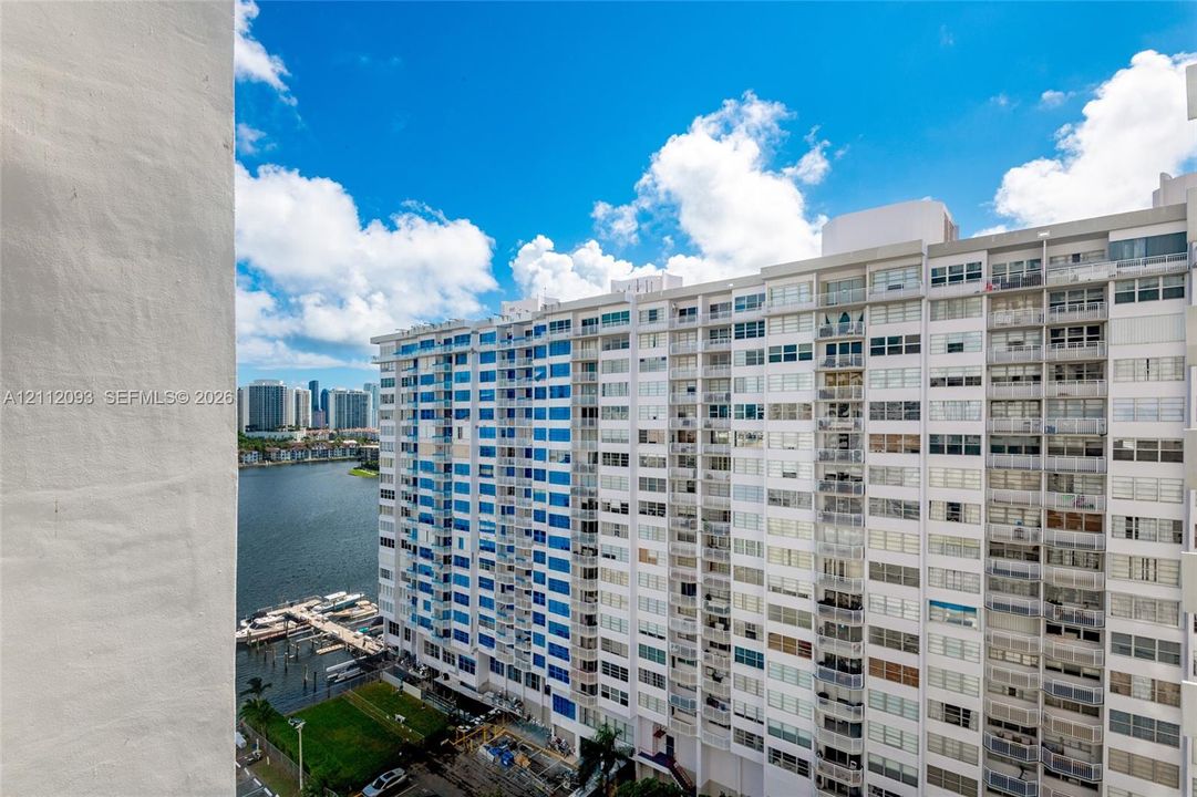 High-rise exterior featuring integrated balconies, floor-to-ceiling windows, and white masonry cladding, overlooking a coastal waterway and dock area