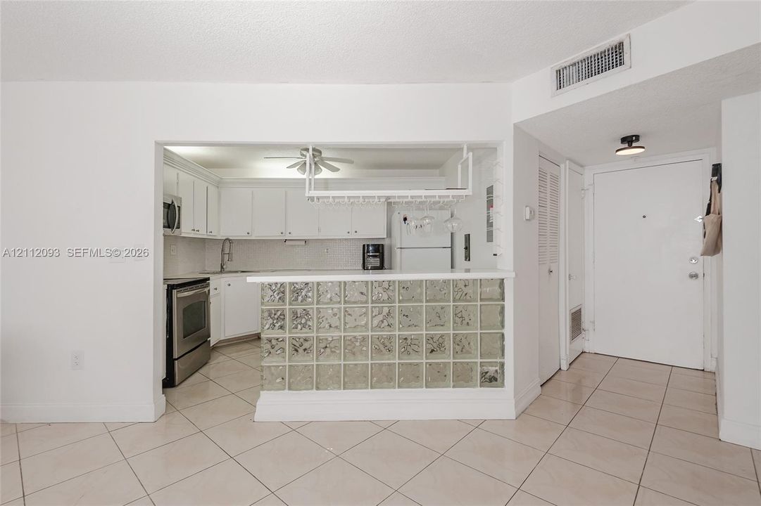 Kitchen featuring white cabinetry, stainless steel appliances, a glass-block breakfast bar, and a hanging stemware rack over ceramic tile flooring
