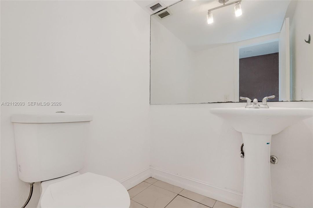 Bathroom featuring a pedestal sink, dual-handle chrome faucet, wall-spanning vanity mirror, multi-light bar fixture, and tile flooring