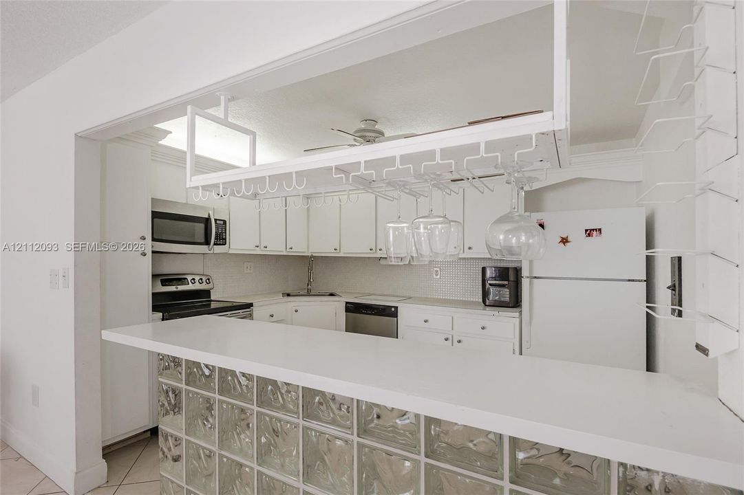 Kitchen featuring white cabinetry, solid-surface breakfast bar, glass block base, and built-in overhead stemware rack