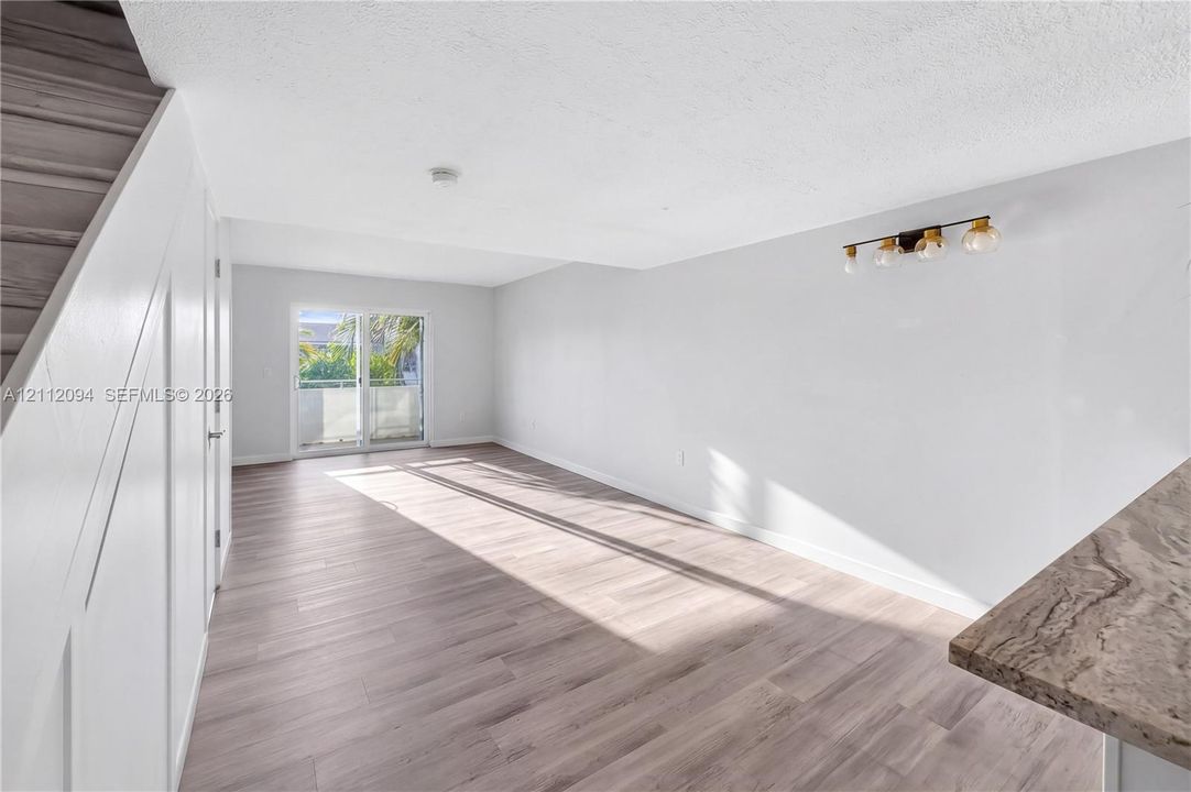 Open-concept interior featuring wood-finish flooring, sliding glass patio doors, stone-finish countertops, and multi-bulb wall lighting