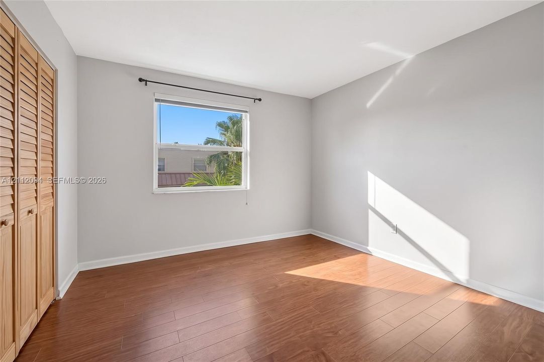 Room featuring wood-finish flooring, neutral wall paint, and a built-in closet with louvered wood doors