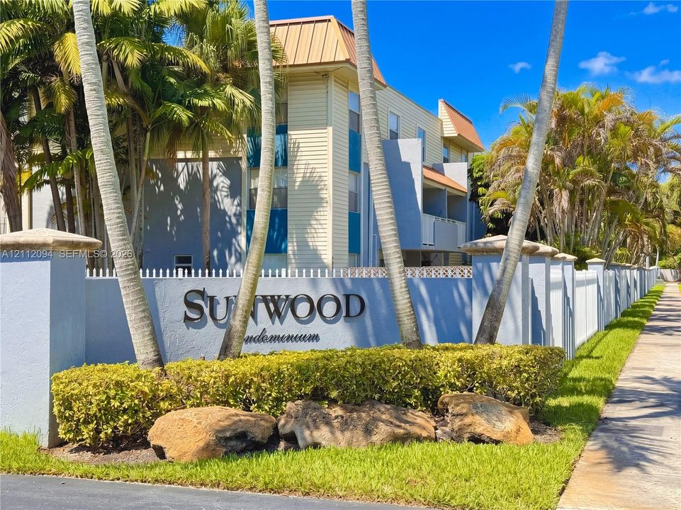 Multi-story building exterior featuring horizontal siding, metal roofing, masonry perimeter wall with integrated signage, and mature palm landscaping