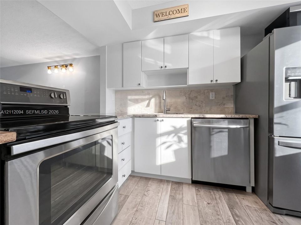 Kitchen featuring white flat-panel cabinetry, stainless steel appliances, neutral stone-finish backsplash, and wood-finish flooring