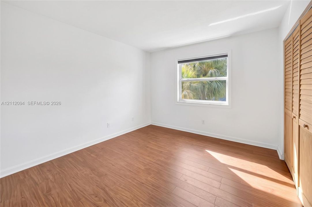 Room featuring wood-finish flooring, white walls, a single-pane window, and louvered closet doors