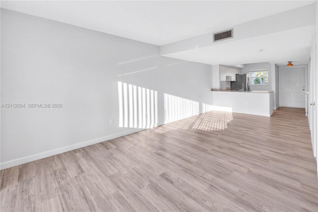 Open-concept interior featuring wood-finish flooring, neutral walls, and a kitchen peninsula with solid-surface countertops