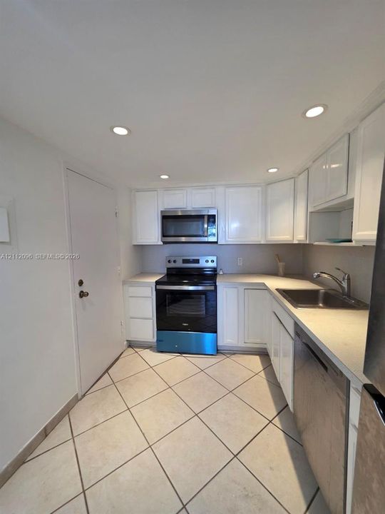 Kitchen featuring white cabinetry, solid surface countertops, stainless steel appliances, recessed ceiling lighting, and large-format tile flooring
