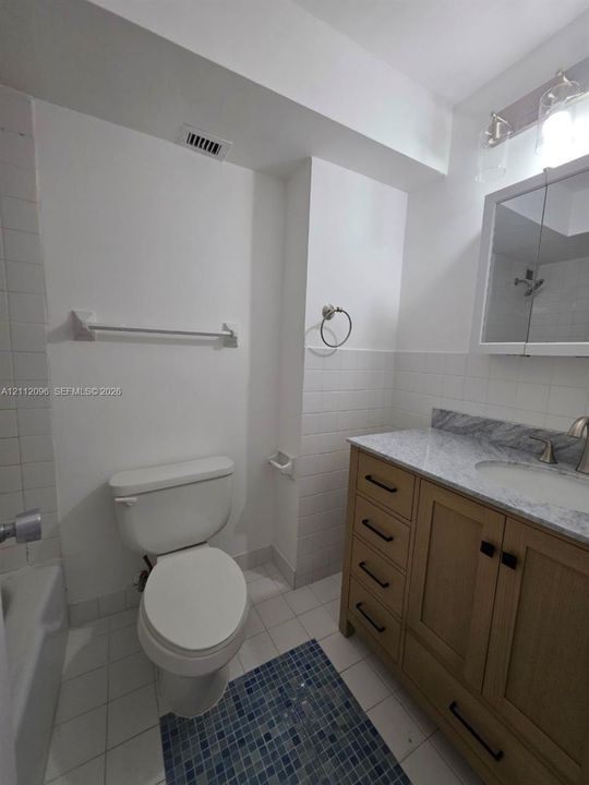 Bathroom featuring a wood-tone vanity with stone countertop, undermount sink, integrated medicine cabinet, and tiled wainscoting