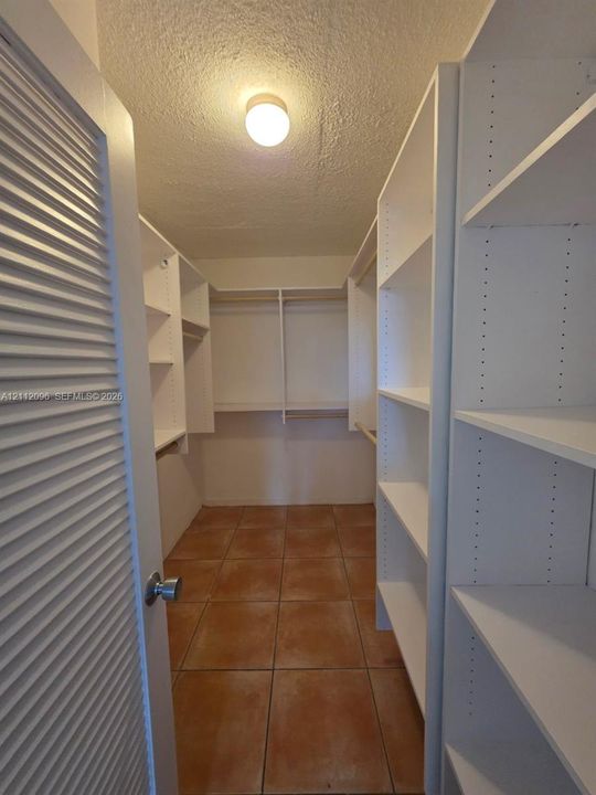 Walk-in closet featuring white built-in shelving, adjustable shelving units, hanging rods, and tile flooring