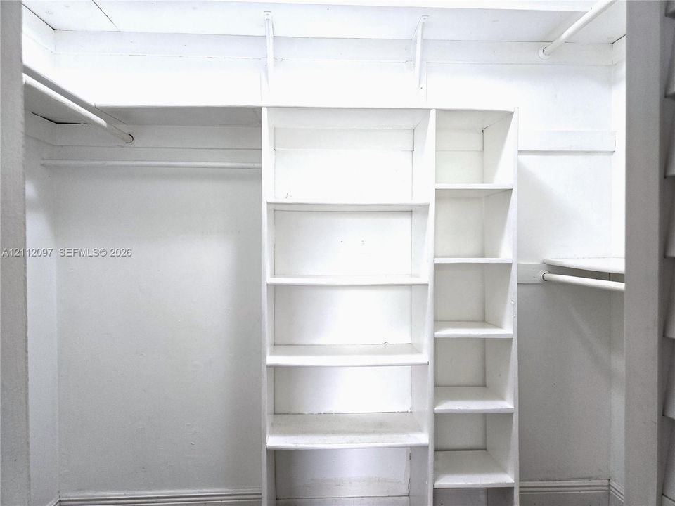 Walk-in closet featuring white built-in shelving units, upper storage ledges, and integrated clothes hanging rods