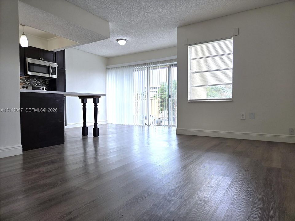 Wood-finish flooring, kitchen peninsula with dark cabinetry, stainless steel microwave, glass sliding door, and neutral wall tones