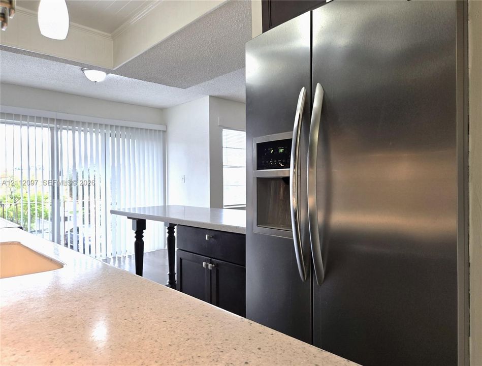 Kitchen featuring stainless steel refrigerator, white solid-surface countertops, dark cabinetry, and sliding glass doors
