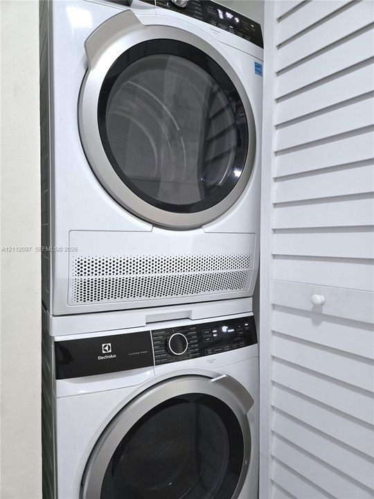 Stackable white front-load washer and dryer unit with digital control panels, enclosed by white louvered doors