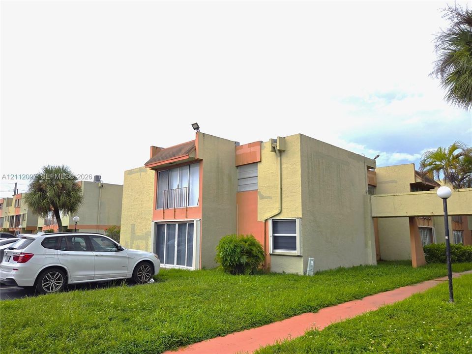 Multi-story exterior with stucco finish, sliding glass doors, upper-level balcony, and covered walkway