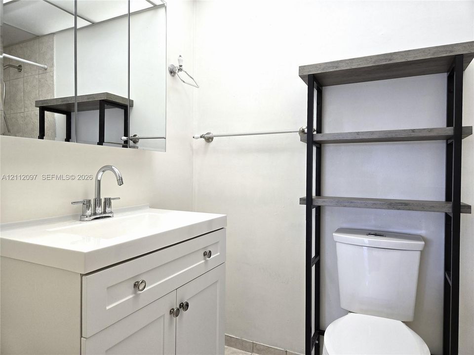 White vanity featuring a rectangular basin, chrome faucet, and integrated storage, paired with a metal and wood-finish wall shelving unit