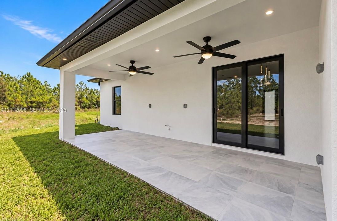 Covered patio featuring large-format tile flooring, dual ceiling fans, recessed lighting, and black-framed sliding glass doors