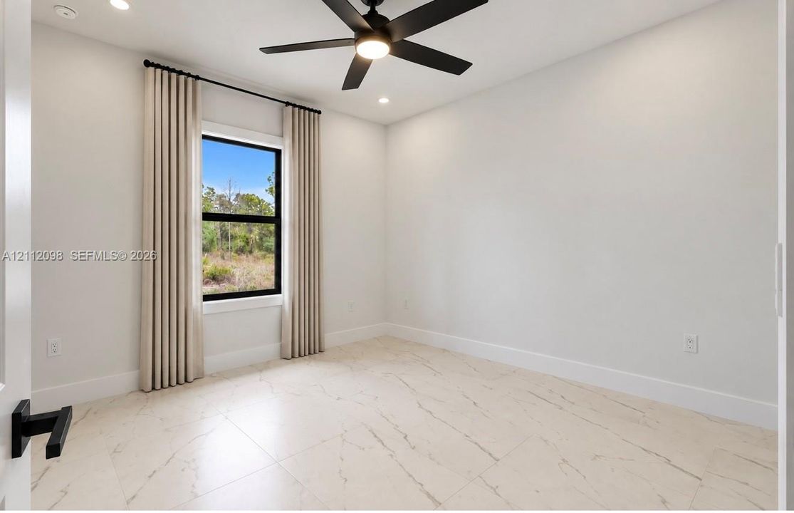Neutral-toned room featuring large-format tile flooring, a matte black ceiling fan with integrated lighting, and a single-hung window with a black frame