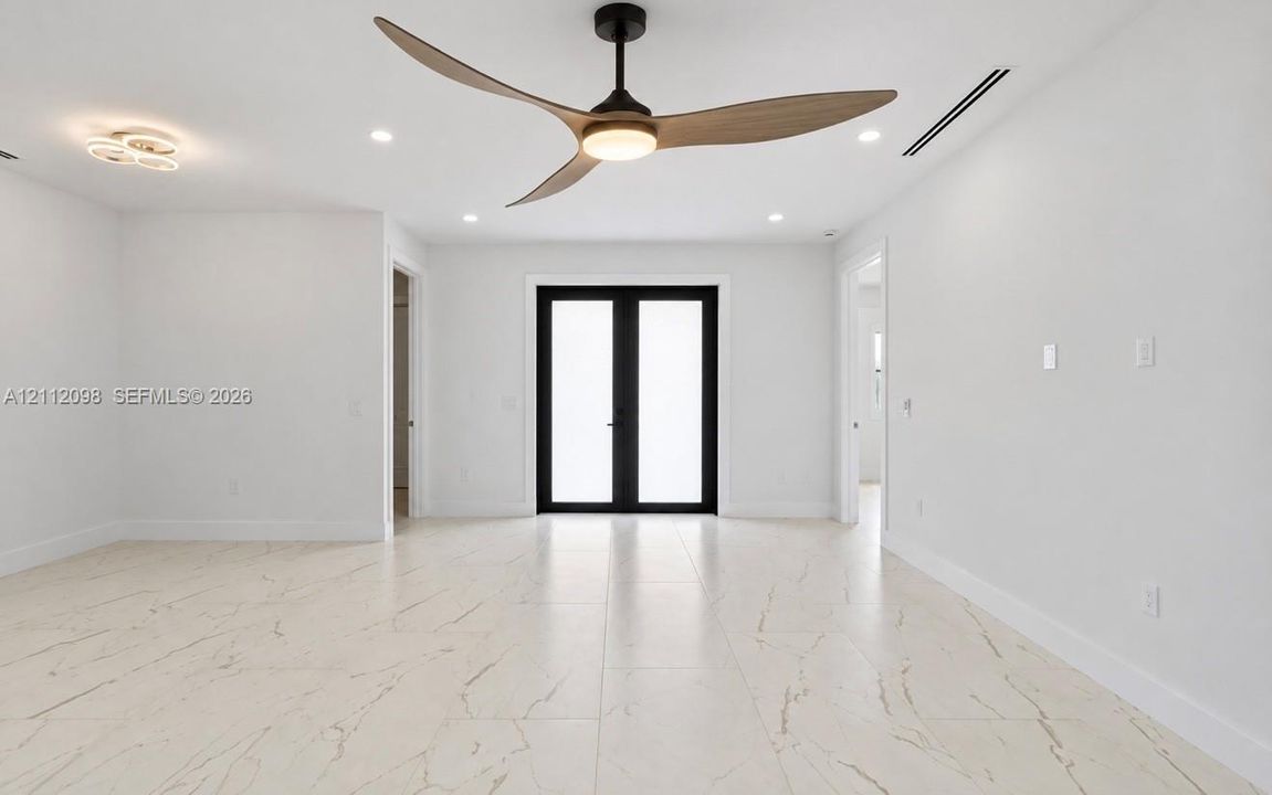 Spacious interior featuring large-format tile flooring with veining, three-blade ceiling fan with integrated lighting, dual glass-paneled exterior doors with black frames, and recessed lighting