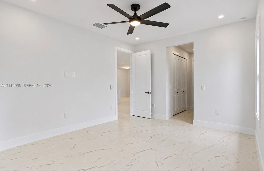 Interior space featuring large-format veined tile flooring, matte black ceiling fan with integrated lighting, recessed lighting, and solid-core panel doors