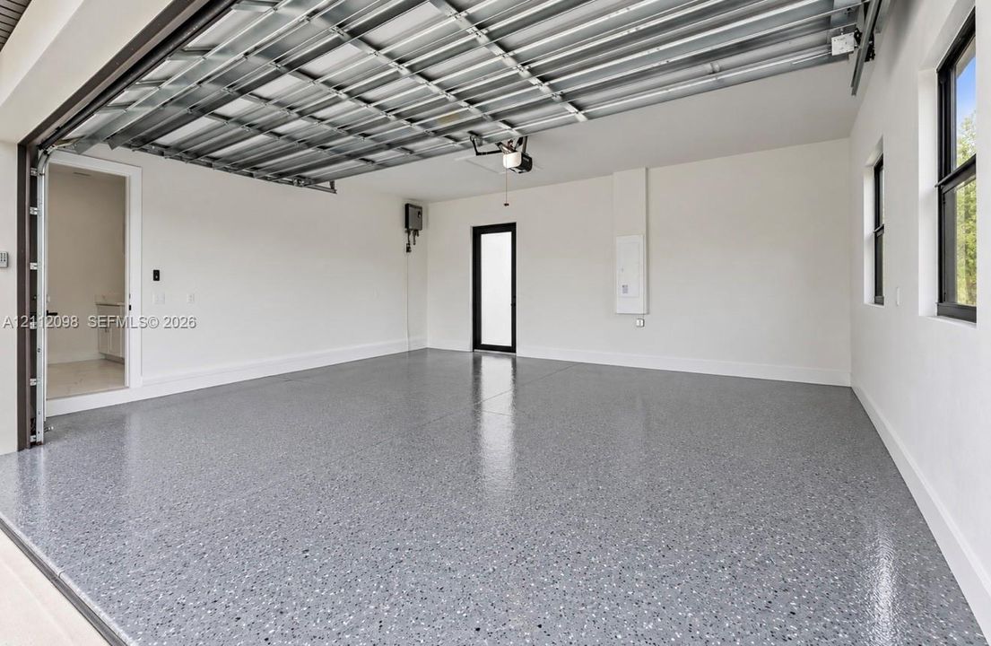 Spacious garage featuring finished epoxy flooring, high-clearance overhead door, smooth-finish walls, and an exterior access door with glass paneling