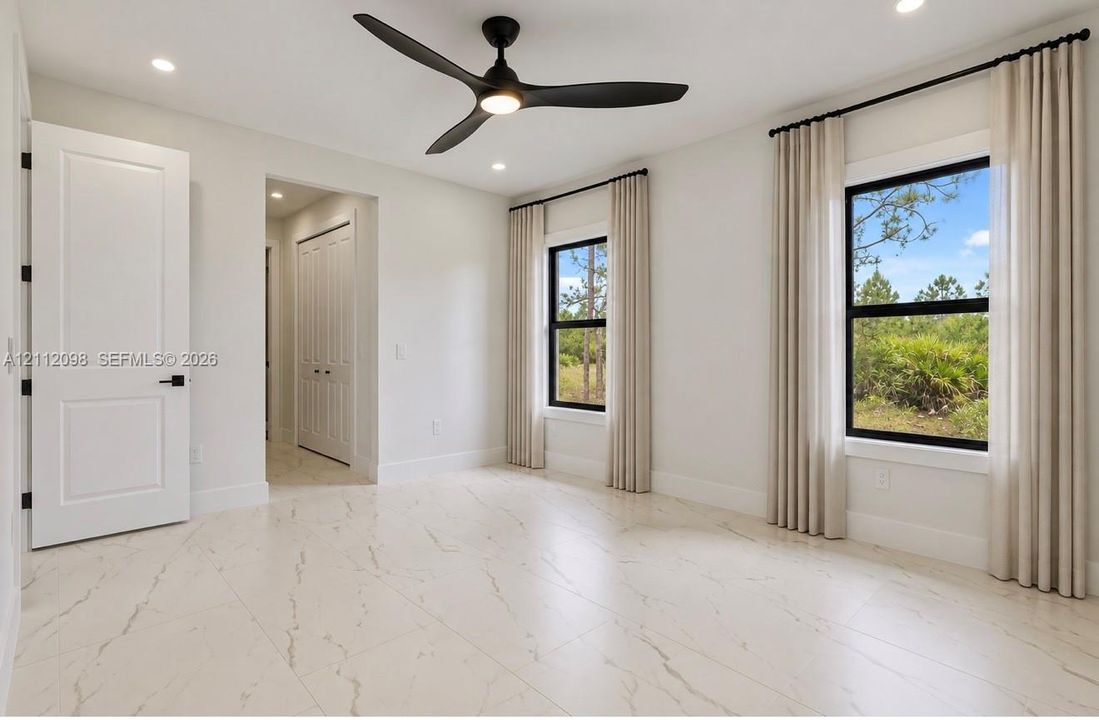 Large-format tile flooring, recessed ceiling lighting, three-blade matte black ceiling fan, and black-framed windows with exterior natural scenery